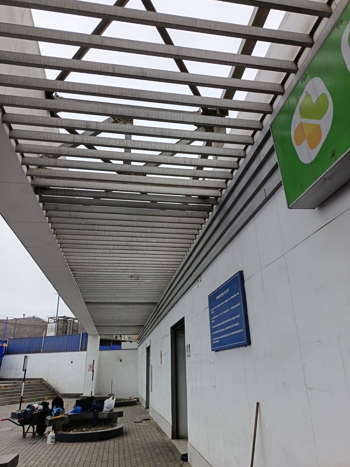 Edificio blanco con una marquesina de listones de madera, un cartel verde y naranja y un panel informativo azul.