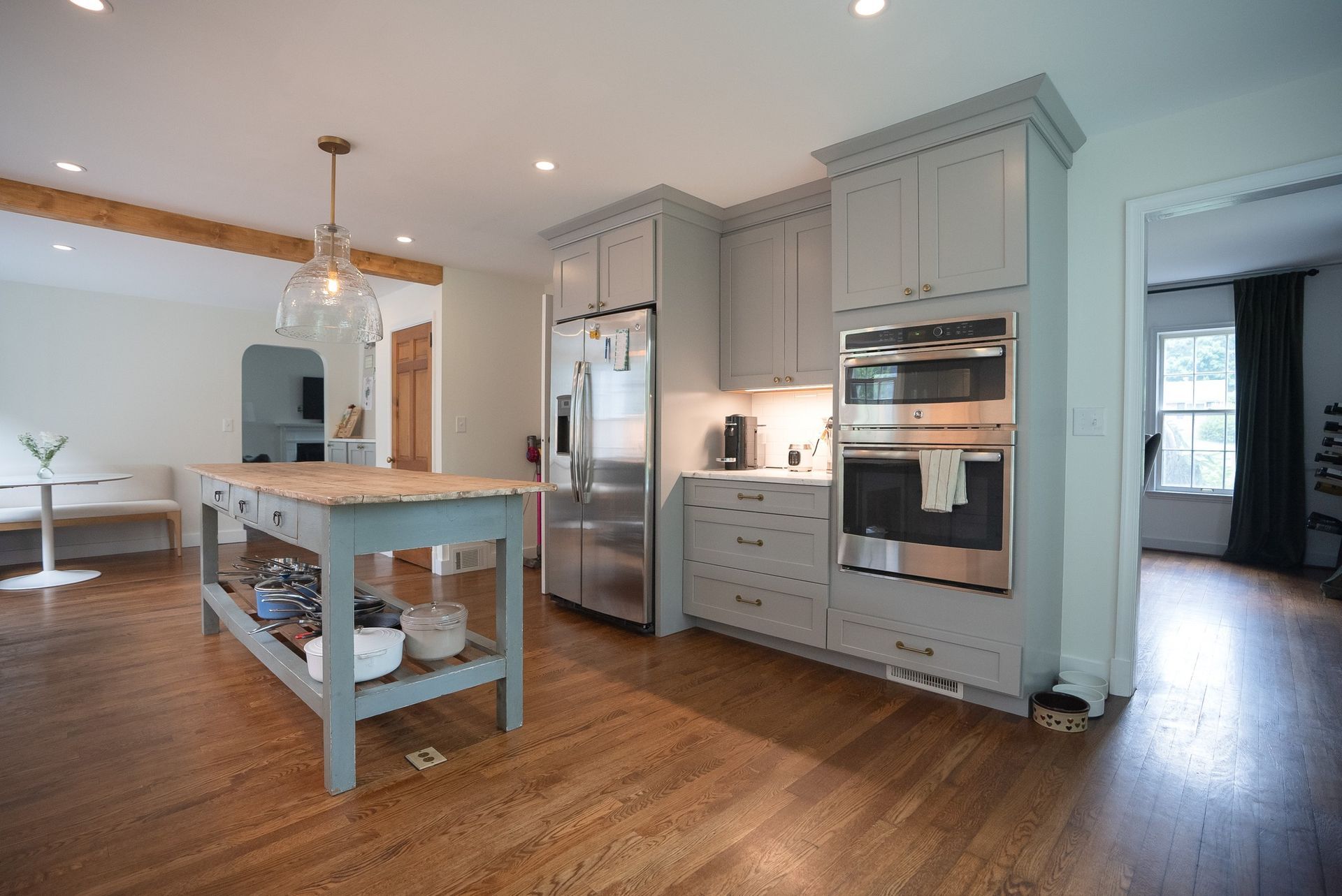 Bright modern kitchen with gray cabinets, white island, stainless appliances, and hardwood floors