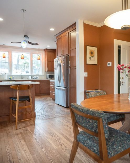 Bright kitchen with wooden cabinets, stainless fridge, island stools, and a dining table in the foreground.