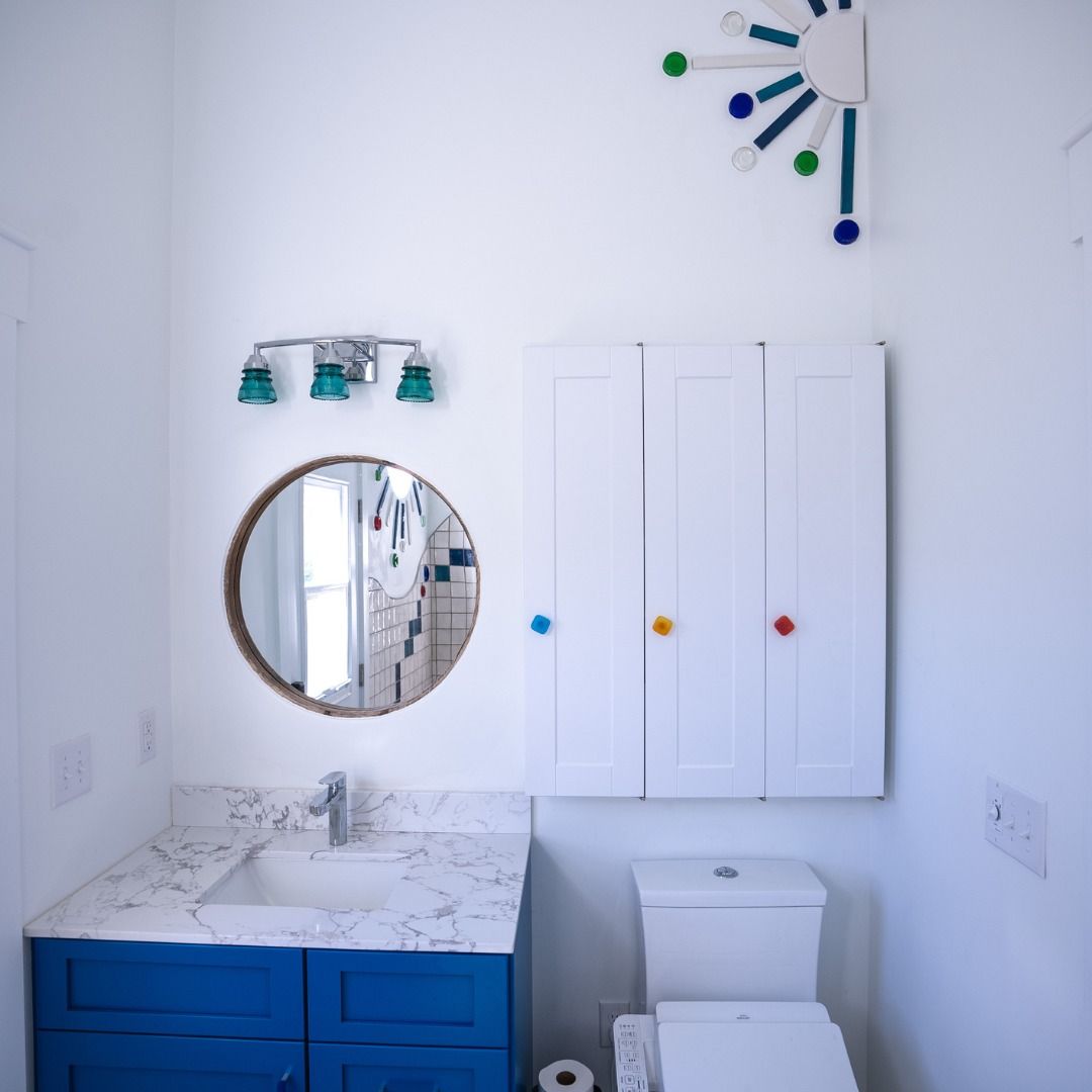 Modern bathroom with blue vanity, round mirror, white cabinet, and colorful wall clock