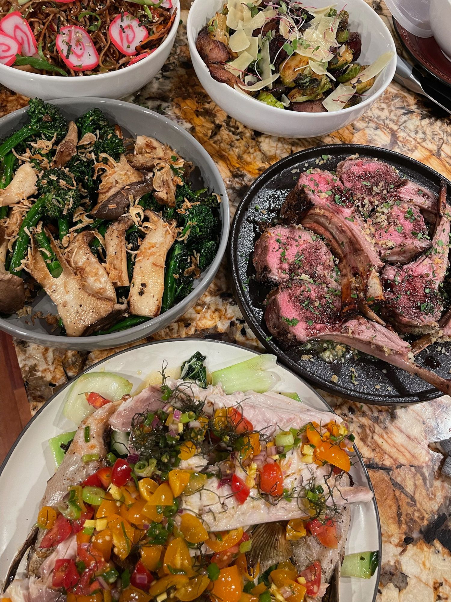 Assorted plated dishes on a granite countertop, including salads and grilled meat with vegetables.