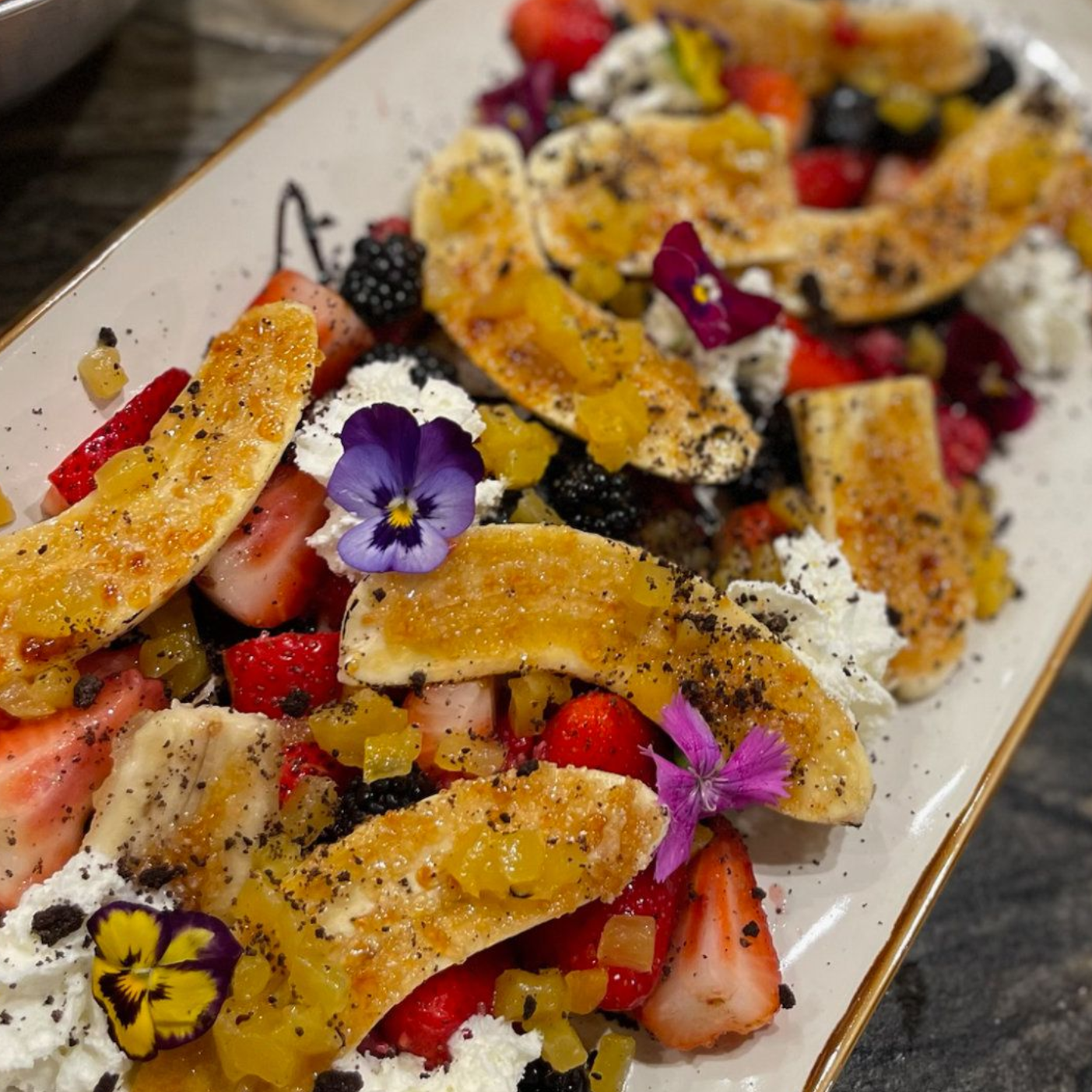 Dessert platter with golden pastry, strawberries, blackberries, powdered sugar, and edible flowers