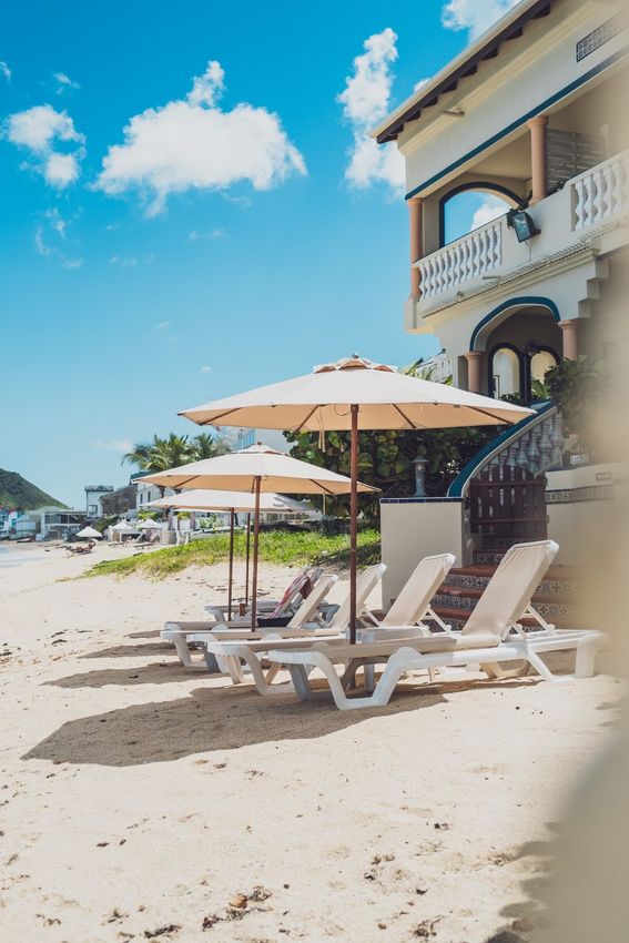 Beach scene with lounge chairs, umbrellas, and a building under a bright blue sky.