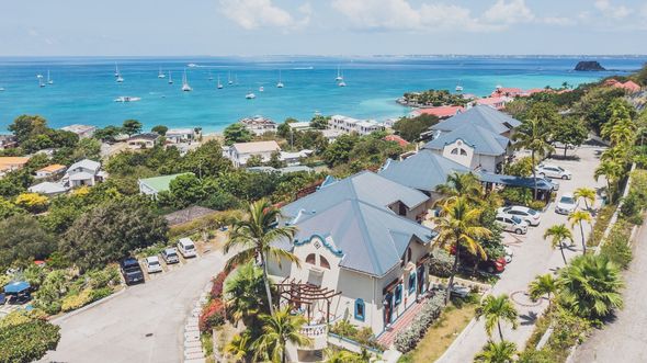 Coastal houses overlooking a turquoise sea dotted with boats. Palm trees line the road.