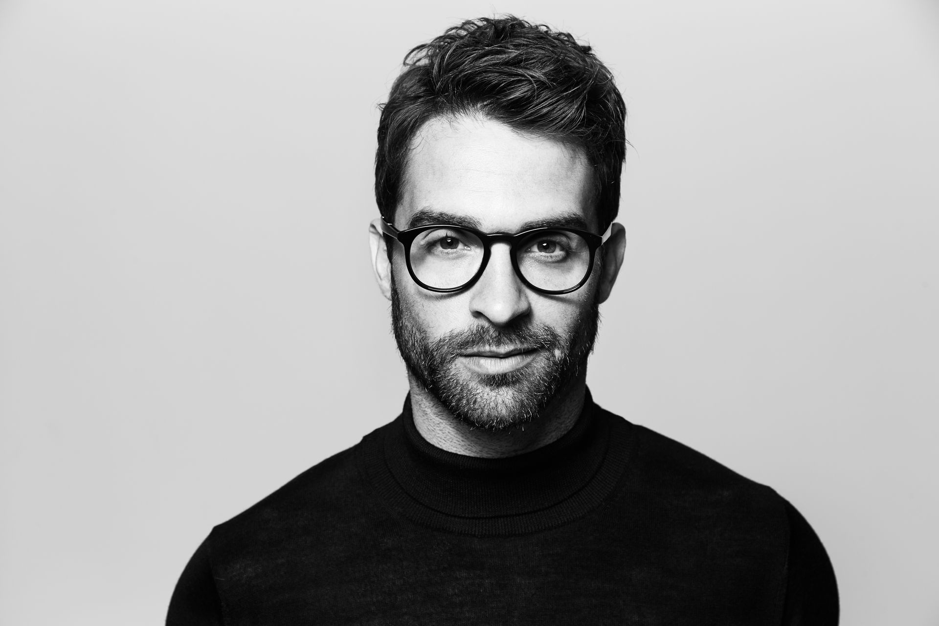 A man with a beard and glasses is wearing a black sweater.