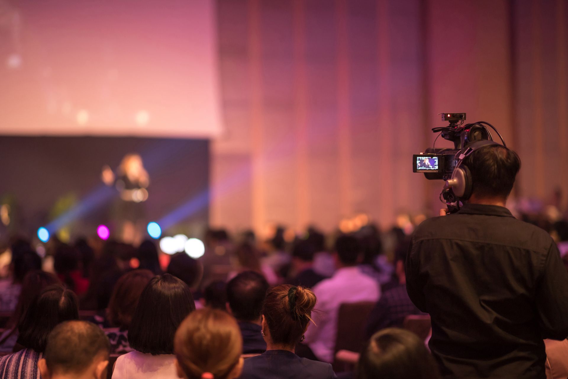 A man is holding a camera in front of a crowd of people at a conference.