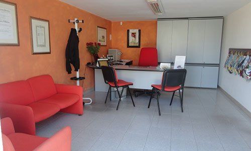 un ufficio con divano,poltrona e sedie rossa, una scrivania, un armadio bianco e pareti color arancione