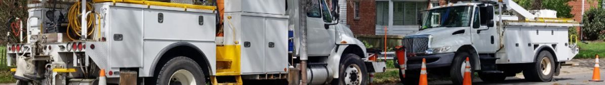 Utility trucks parked on a street with orange cones, possibly for road work or repairs.