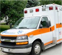 White ambulance with orange stripes and red lights, parked outside.