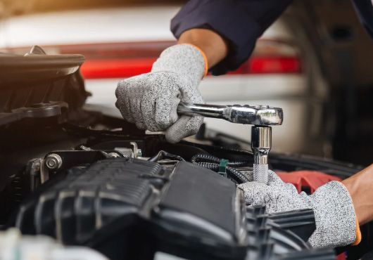 Mechanic using a wrench to work on a car engine, wearing gloves.