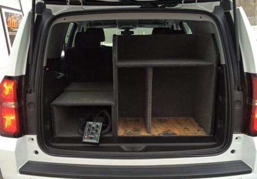 White SUV trunk with custom shelving, holding equipment; gray and brown tones.