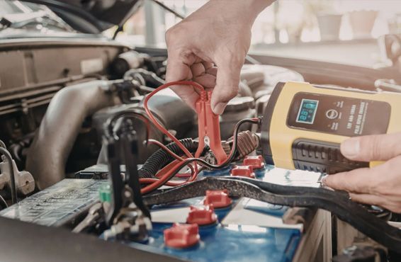 Hands connecting red battery charger cable to a car battery.