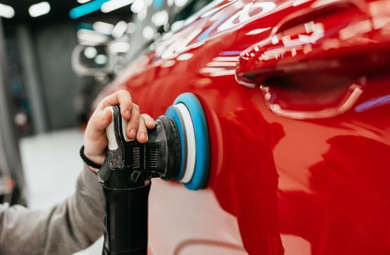 Person polishing a red car with an electric buffer.
