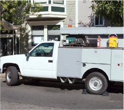 White work truck parked on a street with a building in the background. Tools and equipment visible on the truck bed.