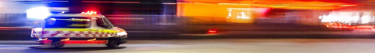 Emergency vehicle with flashing lights speeding on a blurry, colorful road.