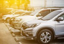 Cars parked in a row at a parking lot, illuminated by sunlight.