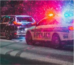 Police car with flashing lights pursuing a dark SUV at night.