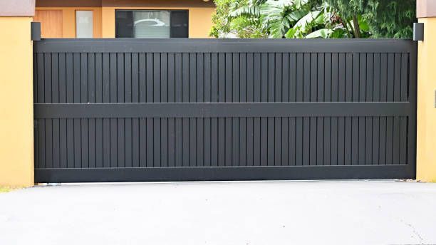 Black slat gate between yellow walls, lush greenery behind.