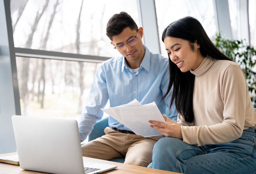Two people reviewing documents beside a laptop in a bright living room