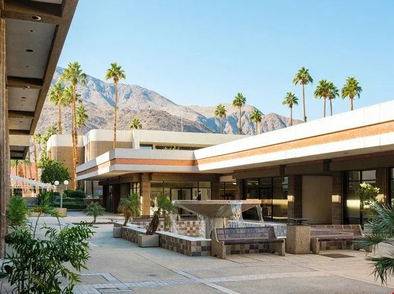 Modern courtyard patio with fire pits, palm trees, and mountain backdrop under a blue sky