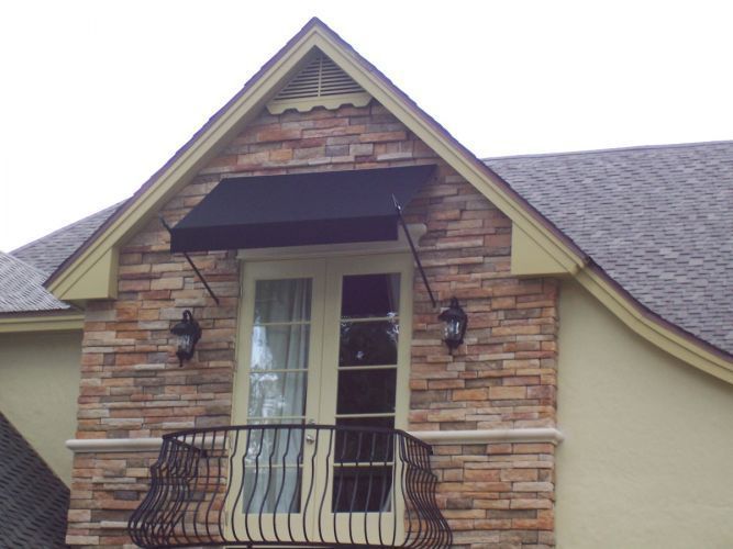 Black awning over a balcony door on a stone and stucco building, with a wrought iron balcony railing.