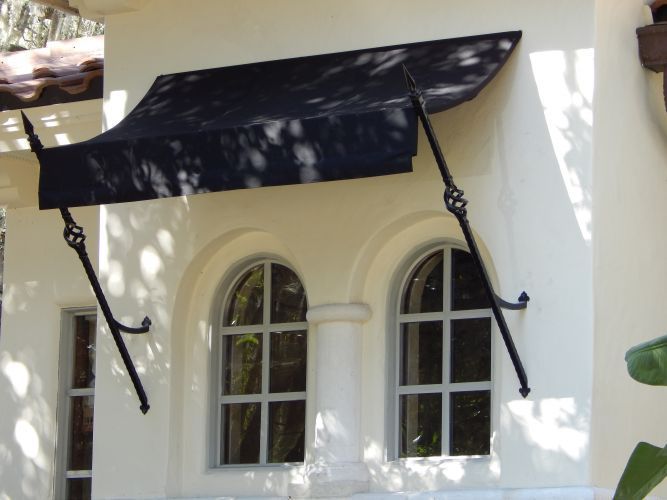 Black awning over two arched windows on a light-colored building, with decorative iron supports.