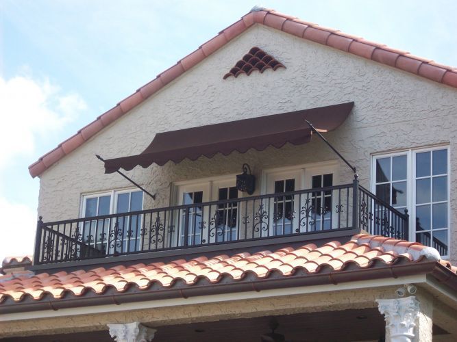 Balcony with ornate black railing and a brown awning. Red tile roof.