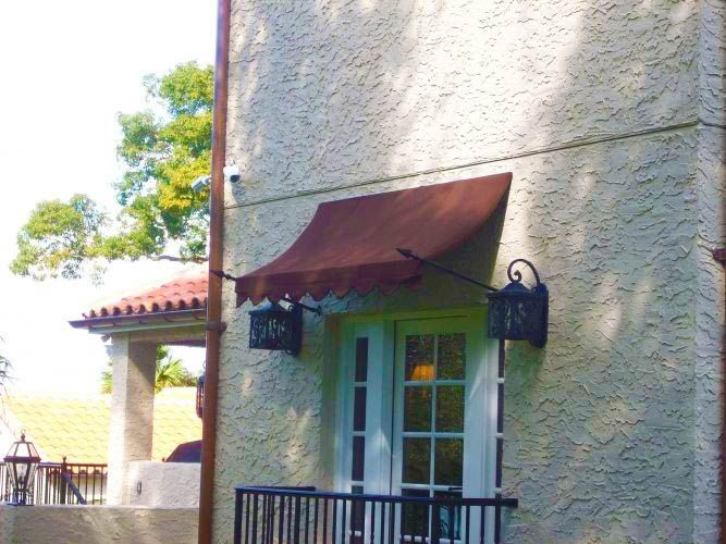 Brown awning over white window on stucco wall, with lanterns.