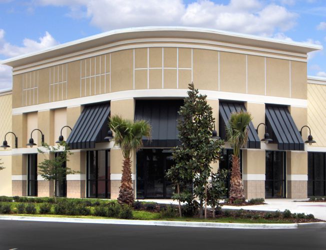 Storefront with beige walls, black awnings, and palm trees.