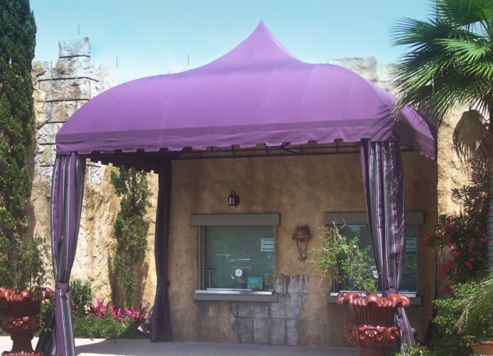 Purple ticket booth with draped curtains, in front of an old stone building.