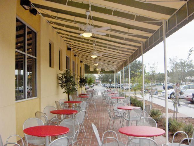 Outdoor cafe with red tables, metal chairs, and a striped awning.