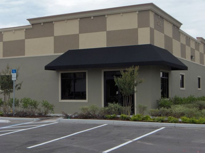 Exterior of a building with checkered tan and brown upper facade, black awning, and parking lot.
