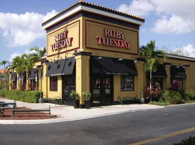 Ruby Tuesday restaurant building, yellow with black awnings, sign, palm trees.