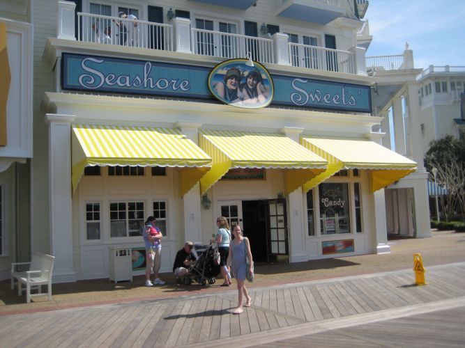 Seashore Sweets shop exterior with yellow awnings, people on boardwalk.