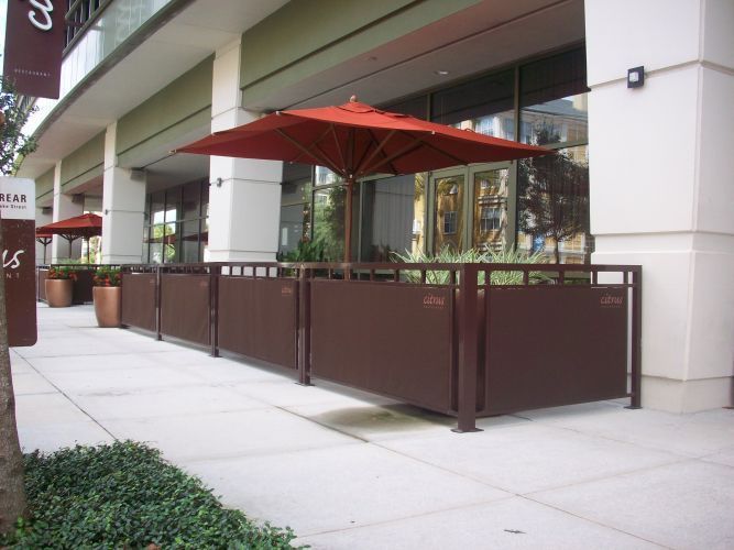 Outdoor seating area with brown barriers, red umbrellas, and a storefront.