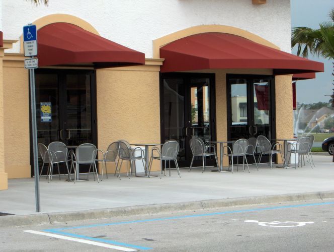 Restaurant exterior with red awnings, outdoor seating, and a handicap parking sign.