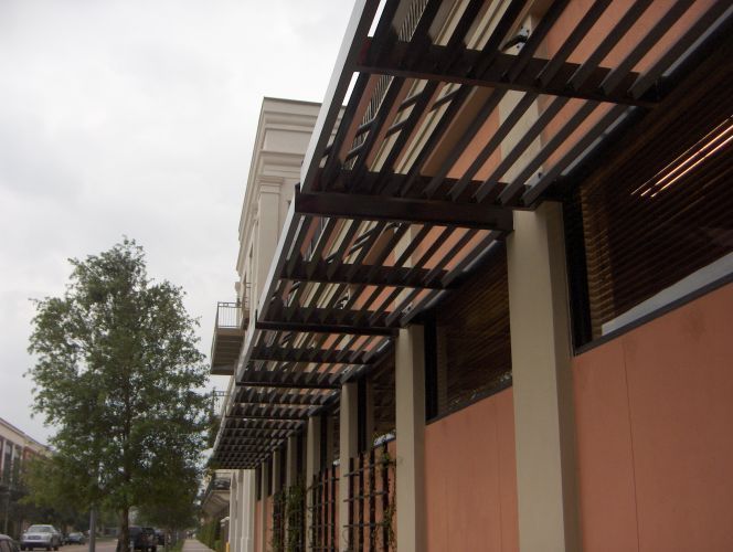Building with a brown metal awning, supported by cream-colored columns, over windows with brown blinds.