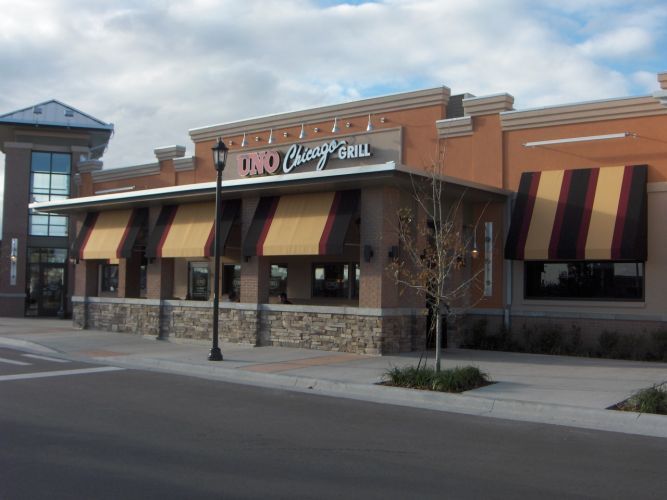 Exterior of a UNO Chicago Grill restaurant with brown and tan awnings and stone accents on a sunny day.
