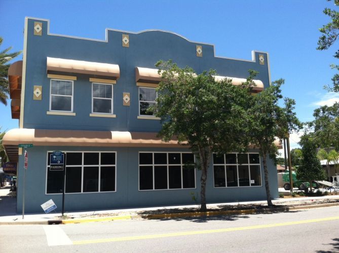 Blue building with awnings and large windows, a street view, and a blue sky.