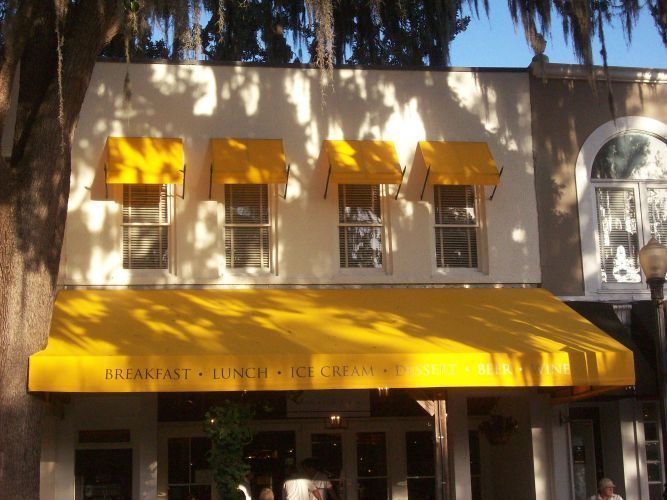 A restaurant with a yellow awning and three smaller yellow awnings above windows; text reads