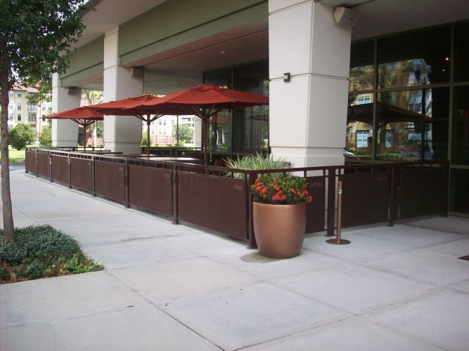 Restaurant patio with brown railing, umbrellas, and seating outside a building.