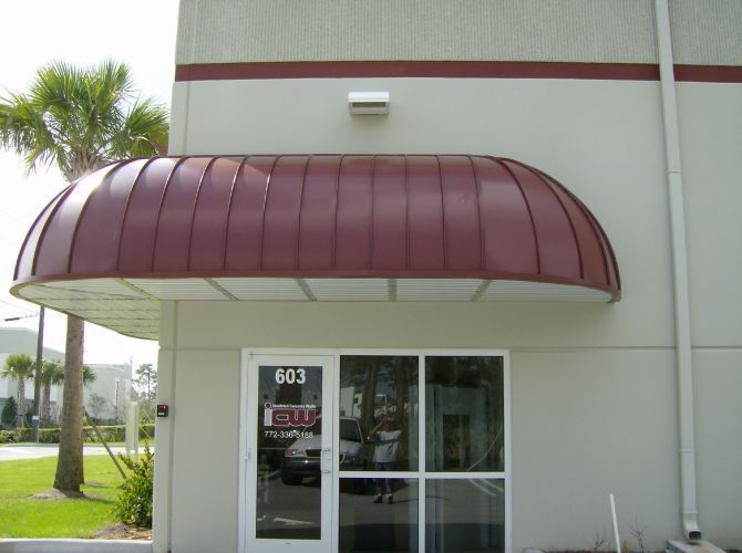 Burgundy-colored metal awning over a storefront entrance with glass door and windows; building is beige.