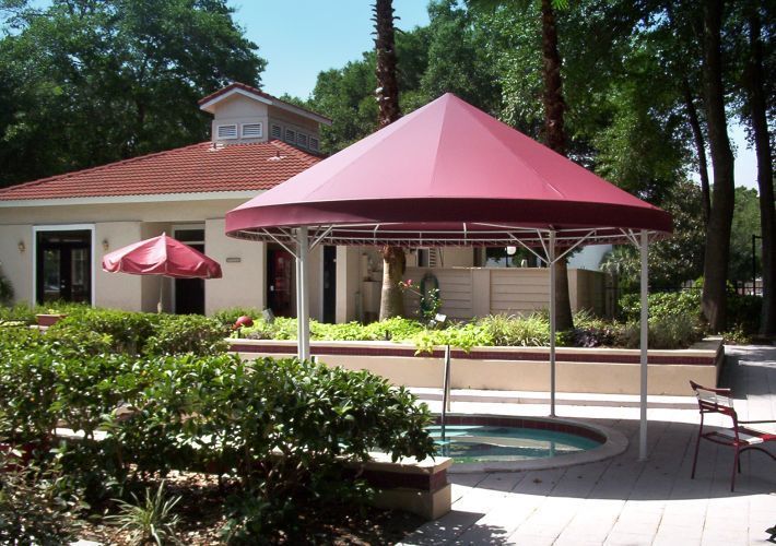 A red-topped gazebo over a hot tub next to a building with a red roof.
