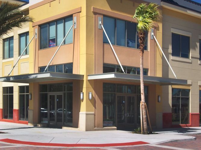 A two-story commercial building with awnings and glass doors on a sunny day; tan and red exterior.