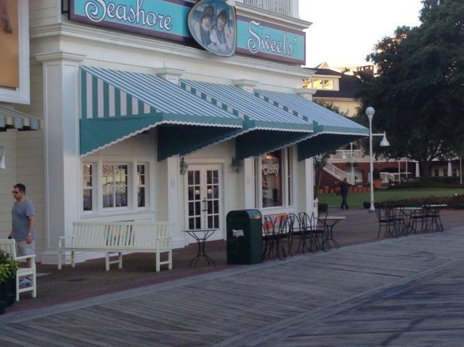 Seashore Sweets shop with teal striped awnings on a boardwalk; a person walks by.