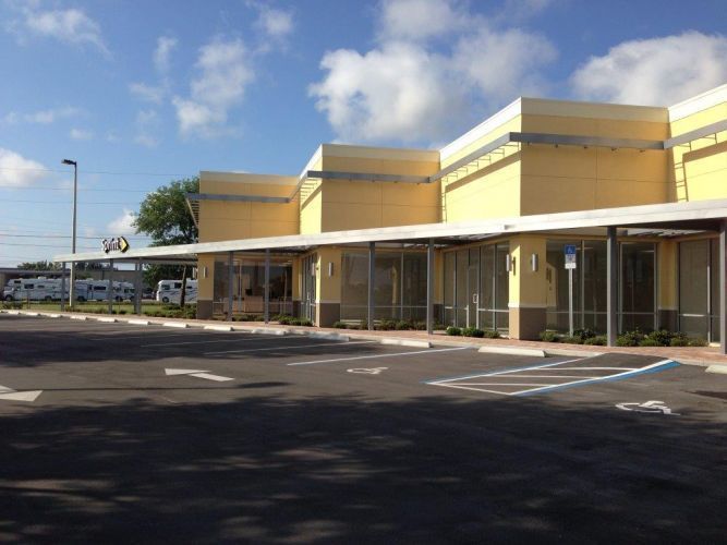 Exterior view of a yellow building with awnings, a parking lot, and cloudy sky.