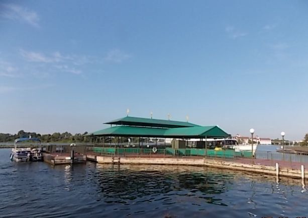 A two-story green building on a pier, surrounded by water, under a blue sky.