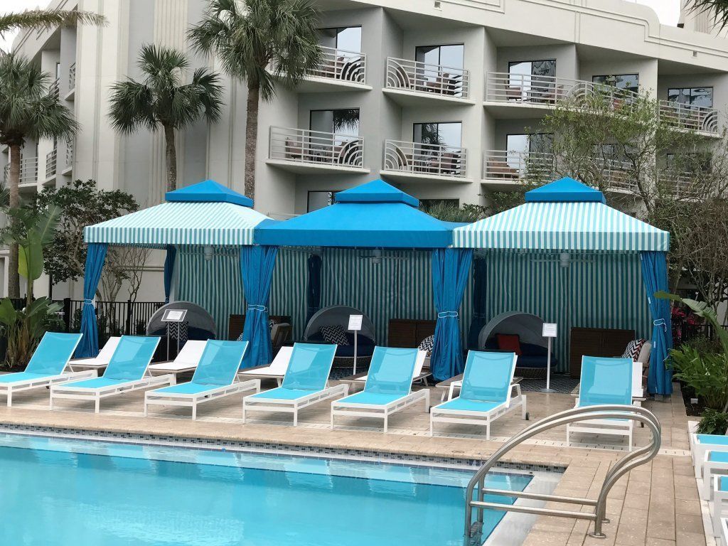 Poolside cabanas with blue and white striped canopies, blue lounge chairs, and a light blue pool.
