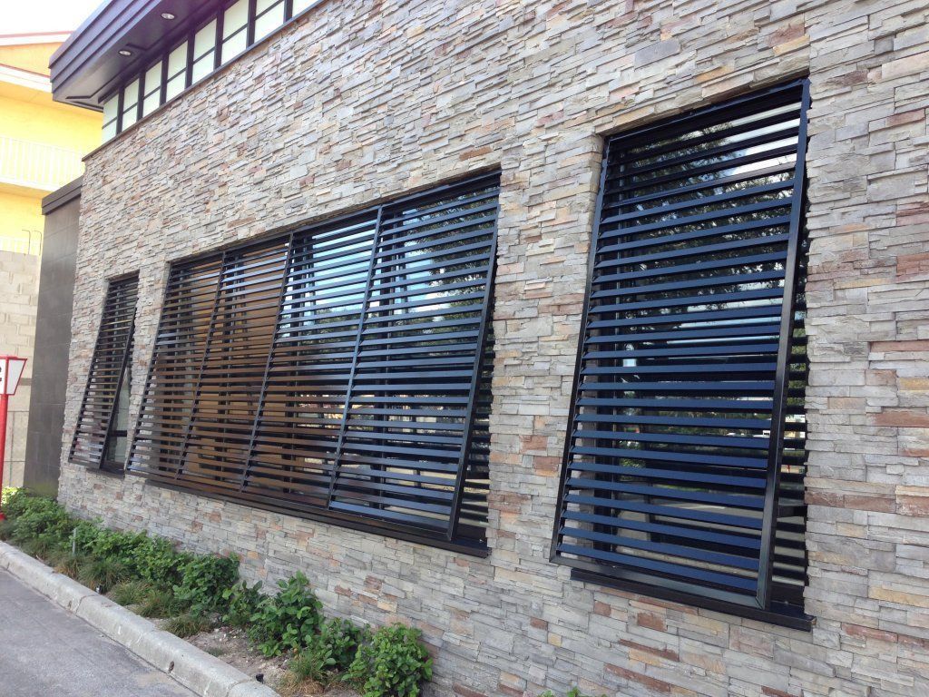 Building exterior with stone facade and black slatted window coverings.