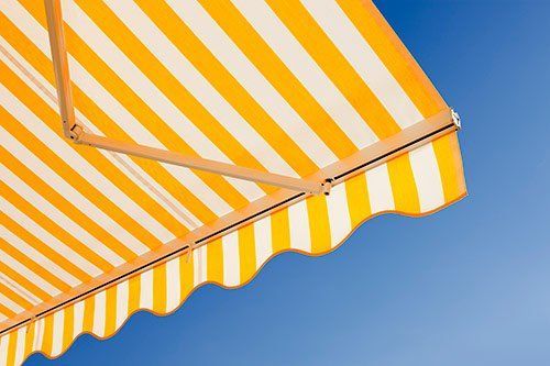 Yellow and white striped awning against a blue sky, partially extended.